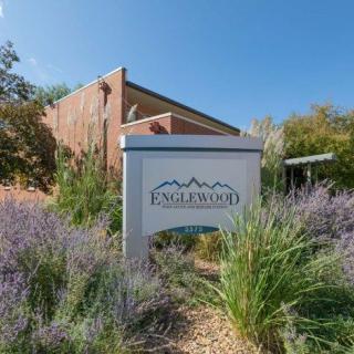 A sign for Englewood surrounded by lush greenery and foliage, with a brick building in the background under a clear blue sky.