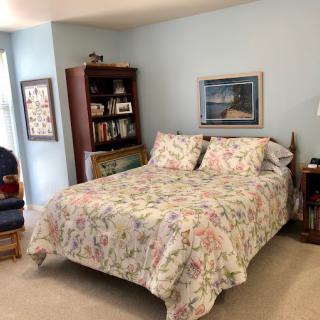 A cozy bedroom featuring a bed with floral bedding, a bookshelf, and wall decorations.