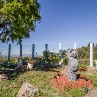 A garden scene with a stone statue surrounded by greenery and a clear blue sky.