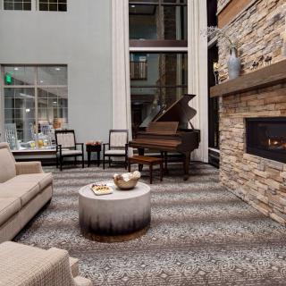 A modern living room with a sofa, coffee table, grand piano, and stone fireplace.