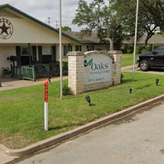 A view of a building with a sign in a residential area, featuring some greenery and a parked vehicle.