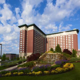 A tall hotel building with well-maintained gardens and vibrant flowers under a partly cloudy sky.