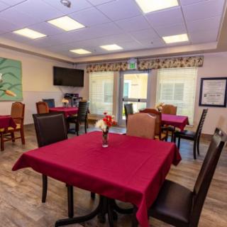 A cozy dining area with neatly arranged tables and chairs, featuring vibrant red tablecloths and decorative elements.