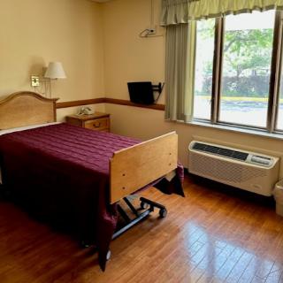 A simple and cozy hotel room featuring a single bed, window, and air conditioning unit.