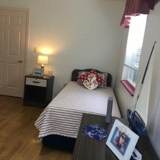 A cozy bedroom with a single bed, nightstand, and a lamp near the window.