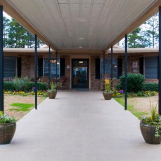 A covered walkway leading to the entrance of a brick building surrounded by greenery.