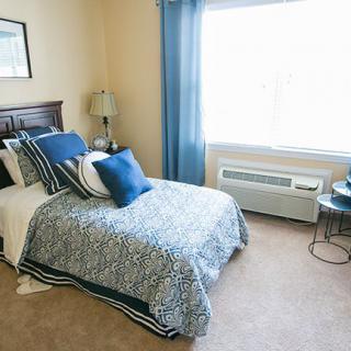 A cozy bedroom with a neatly made bed, blue and white bedding, and a window with blue curtains.