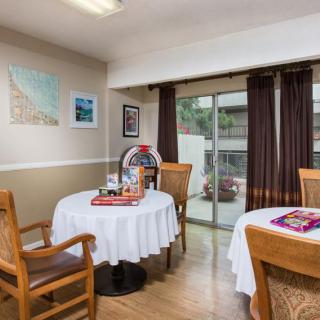 A cozy dining area with round tables and wooden chairs, featuring decorative elements and large windows with curtains.