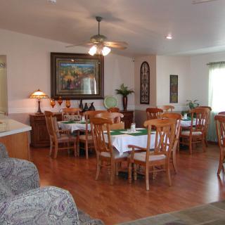 A cozy dining area with wooden tables and chairs, featuring a ceiling fan and artwork on the walls.