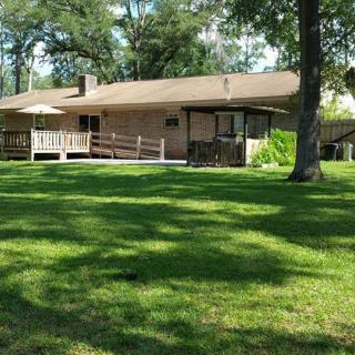 A cozy house with a spacious green lawn and a wooden deck, surrounded by trees.
