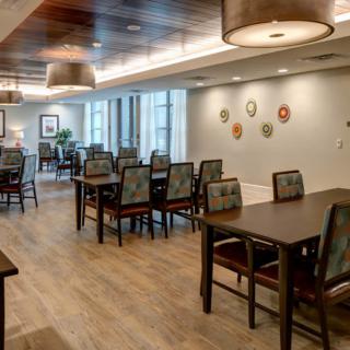 A modern dining area with wooden floors, tables, and chairs under warm lighting.