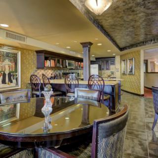A luxurious dining room featuring a polished table and a stylish bar area, adorned with artwork on the walls.