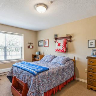 A cozy bedroom with a quilted bed, wooden dresser, and decorative wall items.