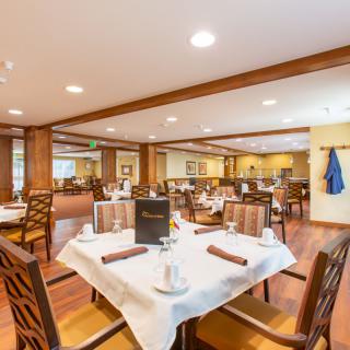 A well-lit restaurant dining area with neatly arranged tables and chairs, featuring elegant table settings.