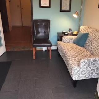 A cozy waiting area with a patterned sofa and leather chair beside a small lamp.