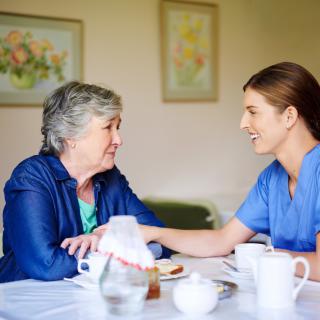 A caregiver providing support to an elderly woman at a table.