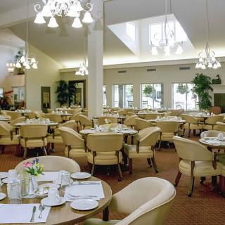 A spacious dining area with neatly arranged tables and chairs, illuminated by elegant chandeliers.
