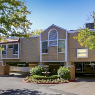 A modern residential building with landscaped surroundings and a driveway, set against a clear blue sky.