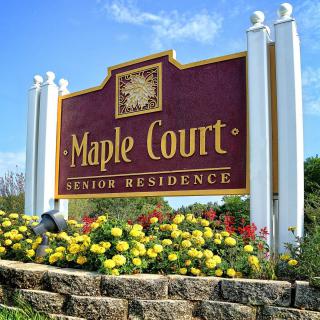 Entrance sign for Maple Court Senior Residence surrounded by colorful flowers.