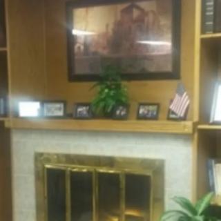 A cozy office setting with a fireplace, bookshelves, and decorative items including artwork and an American flag.
