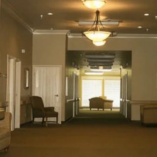A dimly lit hallway with chairs along the walls and a distant window casting light.