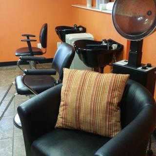 A cozy salon interior featuring chairs, a hairdryer, and washing sinks against an orange wall.