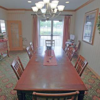 A spacious dining room with a long wooden table and matching chairs, illuminated by a chandelier.