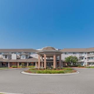 A large residential building with a central entrance and circular driveway on a clear day.
