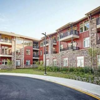 A modern apartment building with stone facades and balconies, surrounded by landscaped areas.