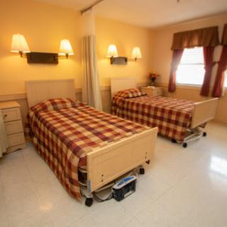 A hospital room featuring two beds with plaid bedding, illuminated by warm indoor lighting.