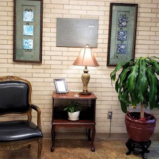 A cozy waiting room corner with a chair, side table featuring a lamp and small plant, adorned by framed wall art.