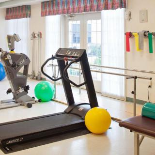 A well-equipped fitness room with a treadmill, exercise bike, therapy balls, and resistance bands.