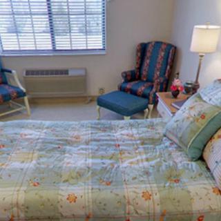 A cozy bedroom with a neatly made bed, colorful chairs, and a lamp by the window.
