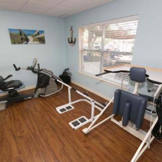 A well-lit exercise room with various gym equipment, including a stationary bike and other fitness machines, on a wooden floor.