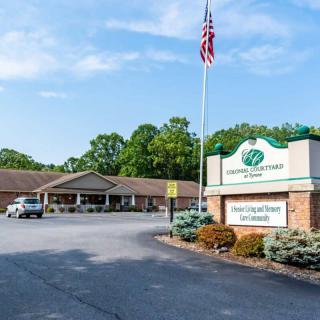 A building with a signboard in front, surrounded by a parking lot and trees, under a clear sky.