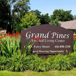 Sign for Grand Pines Assisted Living Center surrounded by greenery.