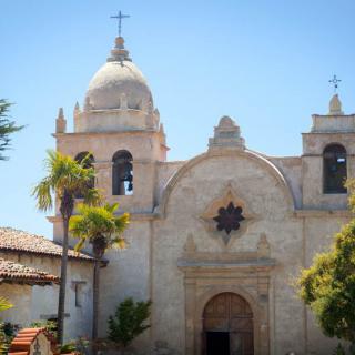 A picturesque church with Spanish colonial architecture, set against a clear blue sky and surrounded by palm trees.