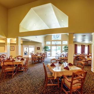 An elegant restaurant dining area with neatly arranged tables and chairs, featuring large windows and a patterned carpet.