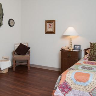 A cozy bedroom with a quilt-covered bed, wooden dresser, and decorative elements on the wall.