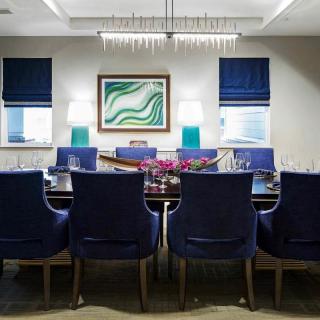 A modern dining room with blue chairs, a chandelier, and contemporary artwork on the wall.