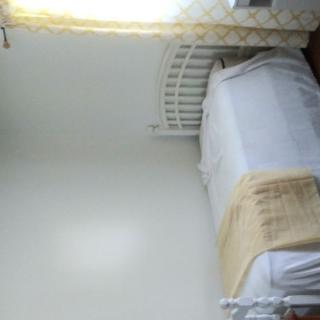 A simple bedroom with a single bed and light curtains.