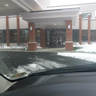 View of a building entrance with snow on the ground, seen from inside a car.