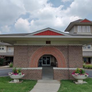 A welcoming entrance to a brick building, adorned with flowers and set against a cloudy sky.
