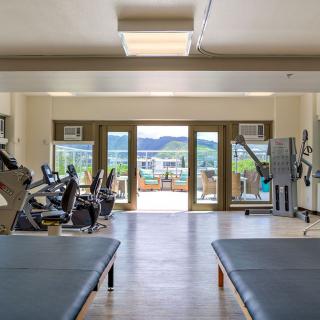 A bright and spacious gym with various exercise equipment, offering a scenic view through large windows.