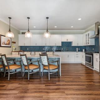 A modern kitchen featuring a large island with bar stools, pendant lighting, and a distinctive blue tile backsplash.