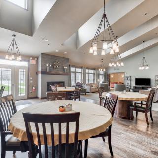 A spacious and modern community dining area with multiple tables, chairs, and chandeliers.