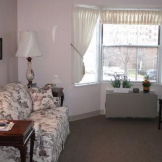 A cozy living room with a floral sofa, table, and lamp near a window with curtains.