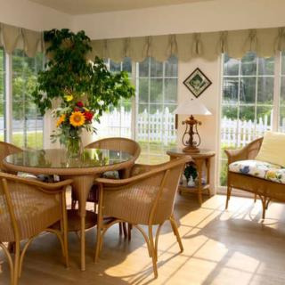 A cozy sunroom featuring a dining area with wicker furniture, a glass table, and an indoor plant bathed in sunlight.