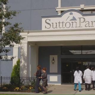 Entrance of Sutton Park building with people in uniforms walking outside.