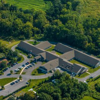 Aerial view of a complex of buildings surrounded by lush greenery and a parking area.